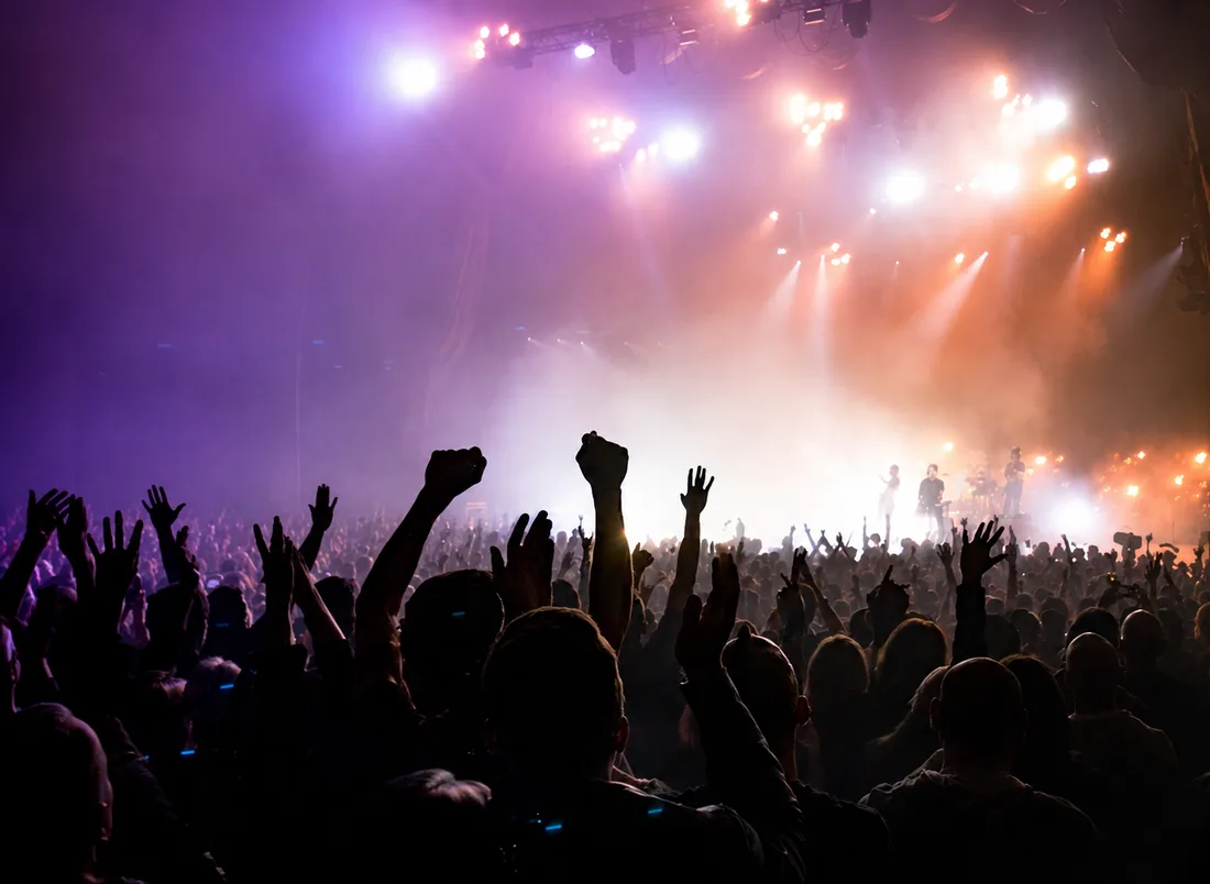 A packed music crowd with hands raised under stage lights
